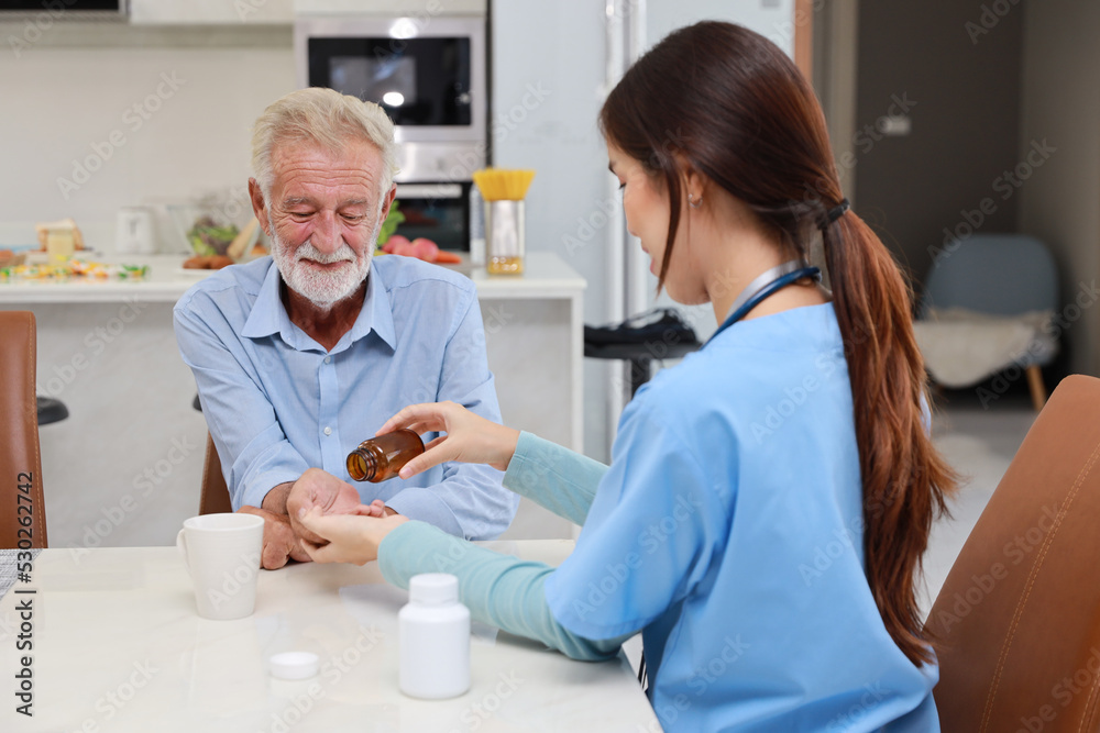 Happy caregiver sitting and helping senior caucasian man taking medicine after breakfast in living room at retirement house. Asian smiling nurse taking good help care and support elder patient at home Happy caregiver sitting and helping senior caucasian man taking medicine after breakfast in living room at retirement house. Asian smiling nurse taking good help care and support elder patient at home