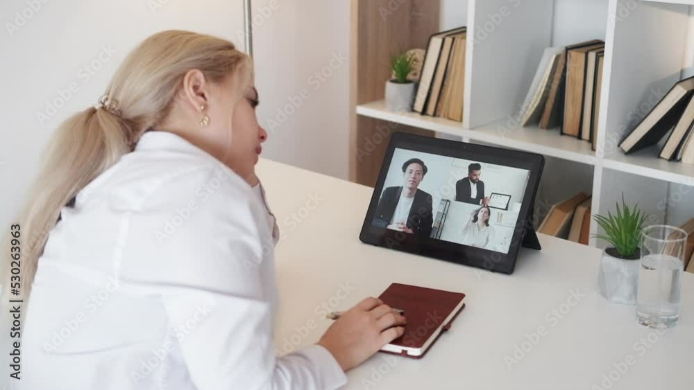 Boring video. Tired woman. Online conference. Exhausted woman falling asleep having virtual meeting on tablet computer in light room interior. Boring video. Tired woman. Online conference. Exhausted woman falling asleep having virtual meeting on tablet computer in light room interior.