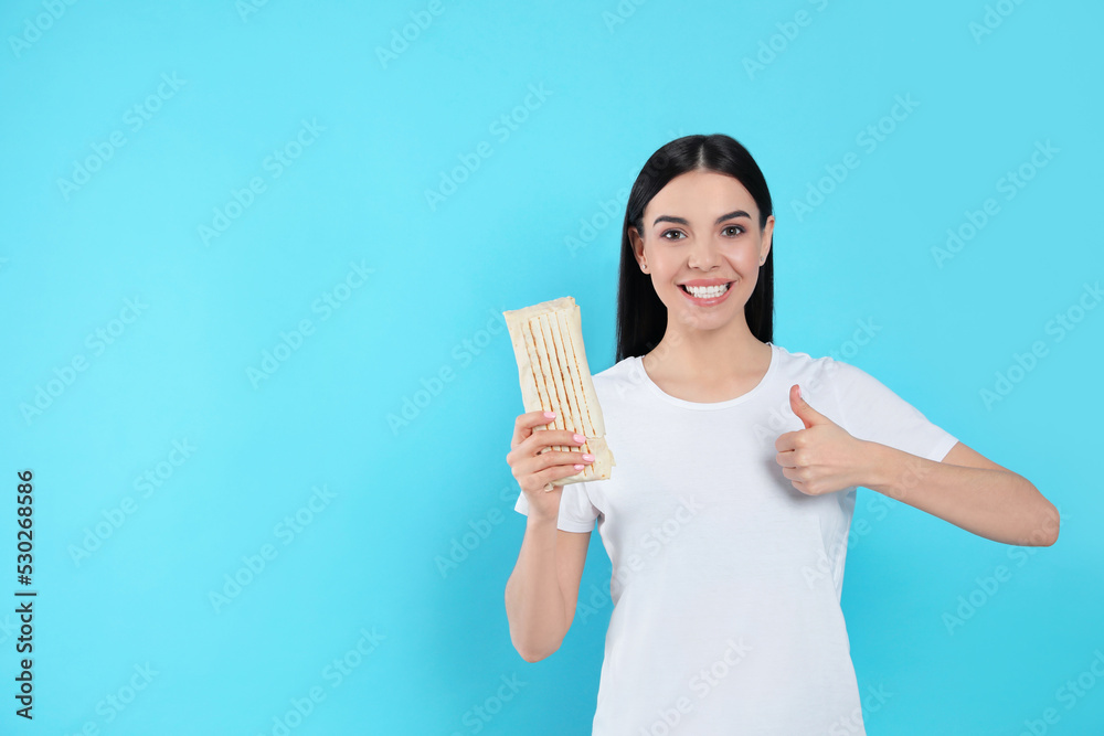 Happy young woman with delicious shawarma on light blue background. Space for text Happy young woman with delicious shawarma on light blue background. Space for text