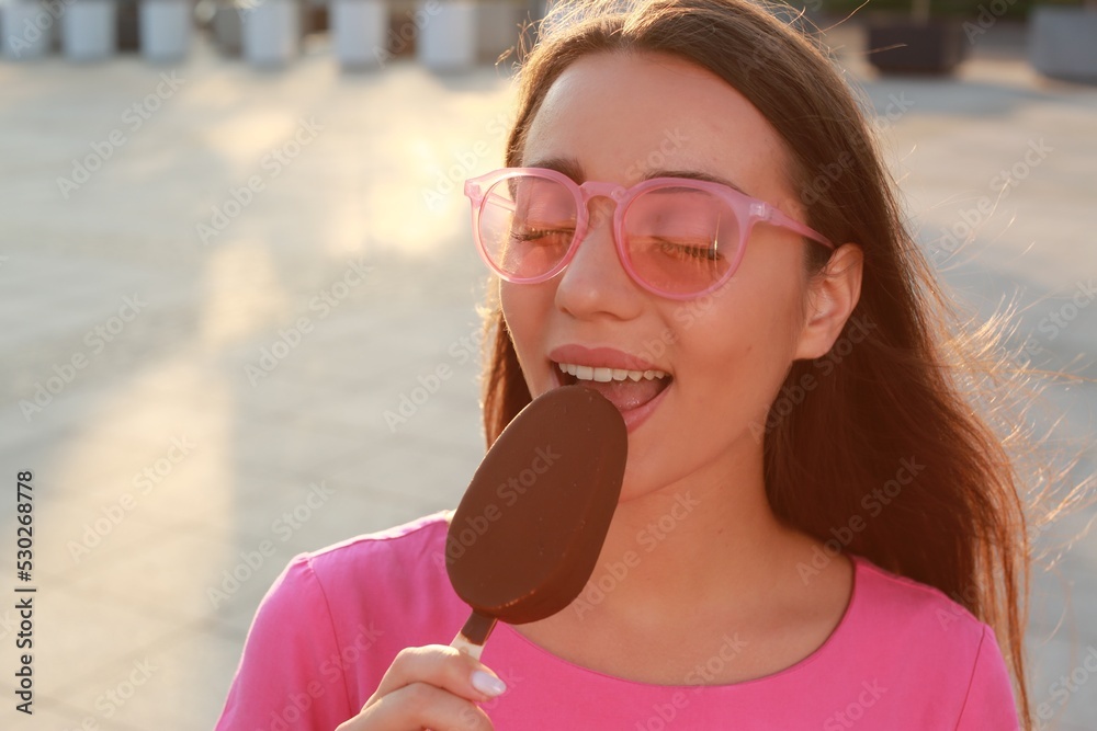 Beautiful young woman eating ice cream glazed in chocolate on city street Beautiful young woman eating ice cream glazed in chocolate on city street