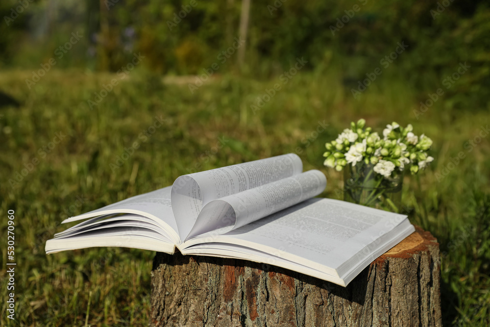 Open book and flowers on tree stump outdoors Open book and flowers on tree stump outdoors