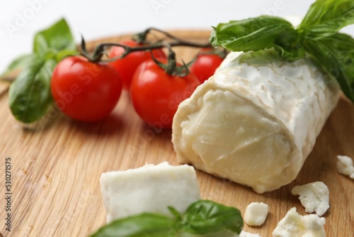 Delicious goat cheese with tomatoes and basil on wooden board, closeup