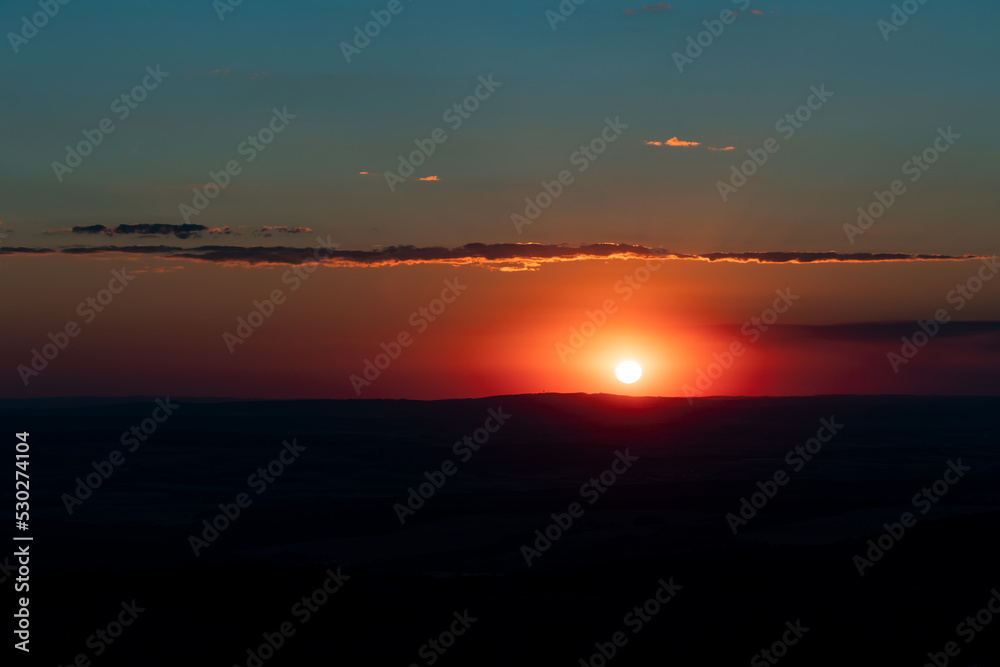 Landscape with sun, glowing sky and clouds. The sun is low, just before setting. View from Feldberg mountain in Hesse, Germany.