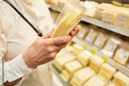Hände einer Kundin halten Packung mit Käse am Kühlregal photo