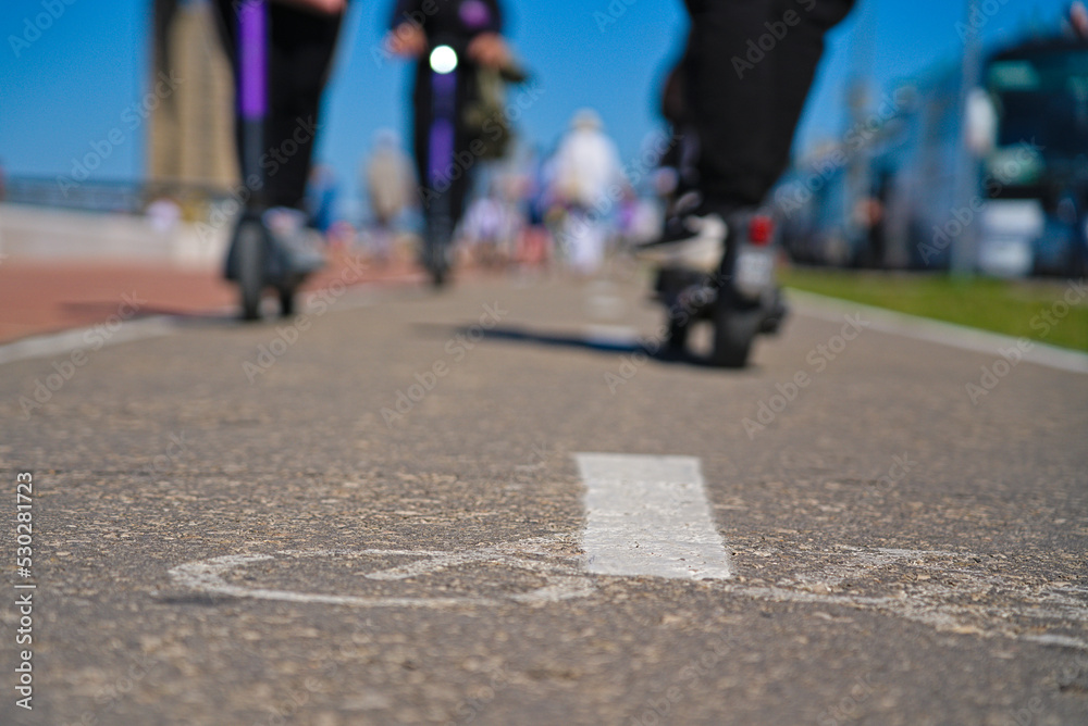 A bike path with markings and scooters passing along it. Scooters on the bike path. Rest on a scooter in the city center. Sports leisure. A bike path with markings and scooters passing along it. Scooters on the bike path. Rest on a scooter in the city center. Sports leisure.