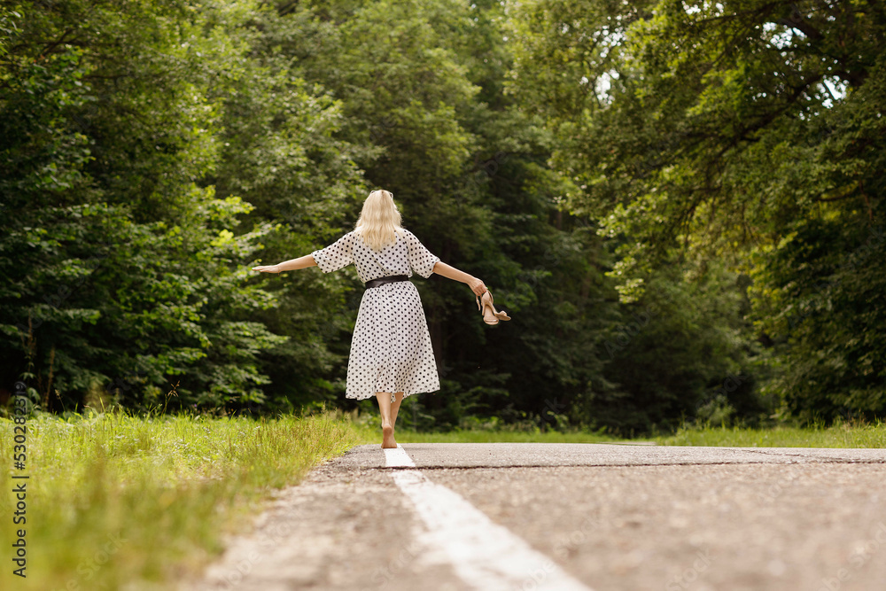 a girl in a white dress with black polka dots walking along a forest road