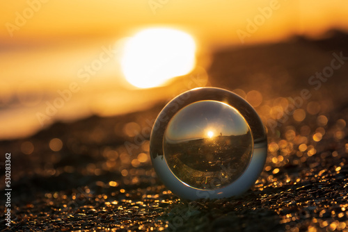 Φωτογραφία Glass lens globe on sandy beach on sea surf and blue sky background at sunset