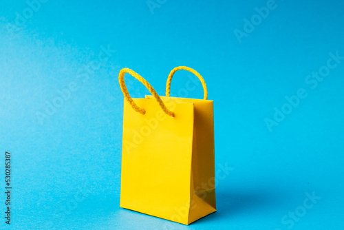 Composition of yellow paper shopping bag on blue background