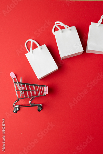 Composition of white bags and shopping cart on pink background