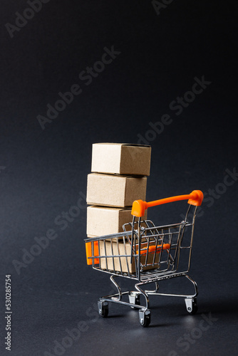Composition of shopping cart with boxes and copy space on gray background