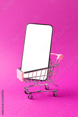 Composition of shopping cart and smartphone with copy space on pink background
