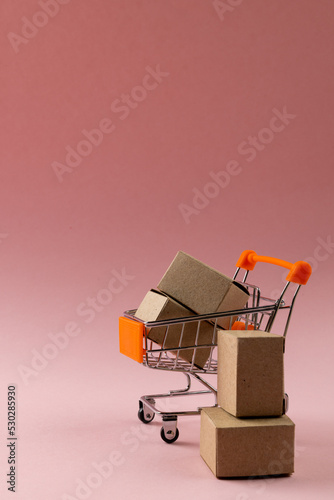 Composition of shopping cart with boxes on pink background