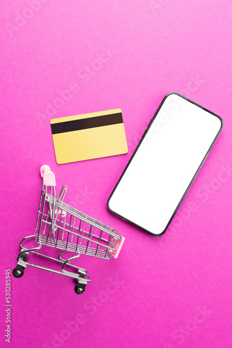 Composition of shopping cart, credit card and smartphone with copy space on pink background