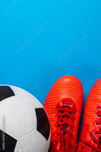 Composition of football and red shoes on blue background with copy space