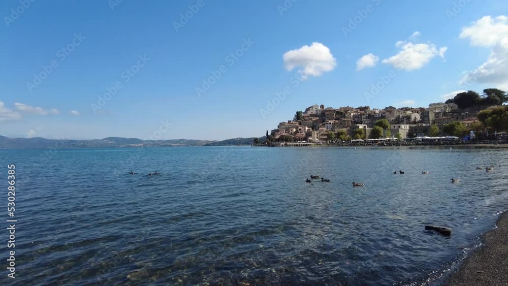 Panning right at Bracciano lake with many birds swimming in clean water and beautiful ancient skyline of medieval village of Anguillara Sabazia Panning right at Bracciano lake with many birds swimming in clean water and beautiful ancient skyline of medieval village of Anguillara Sabazia