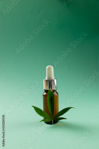 Vertical image of bottle of cbd oil and marihuana leaf on green surface
