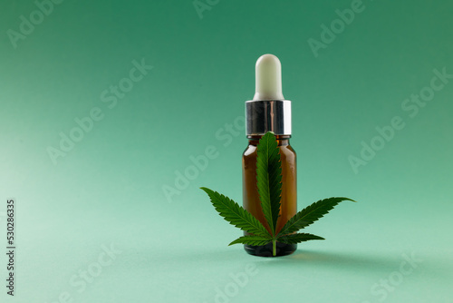 Image of bottle of cbd oil and marihuana leaf on green surface