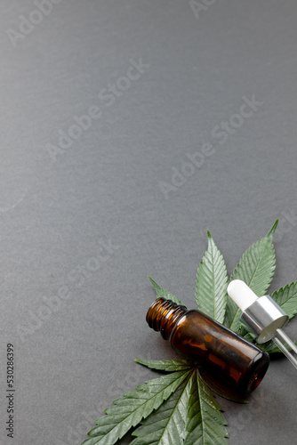 Vertical image of marihuana leaf and bottle of cbd oil on grey surface