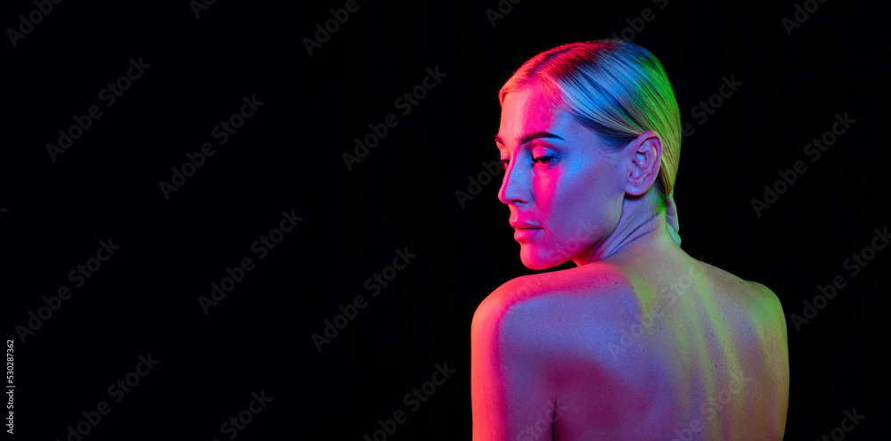 Fototapeta premium Back view of young beautiful woman well-kept skin posing isolated over dark background in purple neon light. Fashion, beauty, health concept