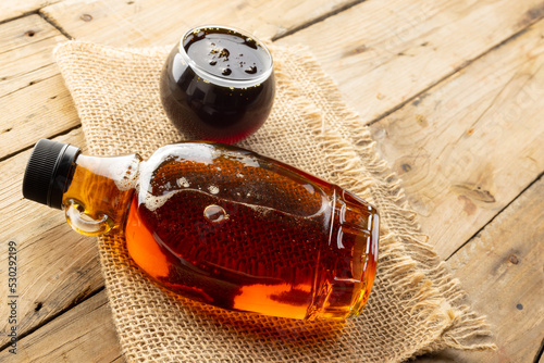 Horizontal image of glass bottle and bowl of maple syrup on sackcloth on wooden table