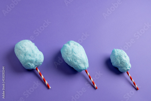 Horizontal image of homemade blue candy floss on three striped sticks, on purple with copy space