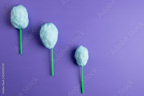 Horizontal image of homemade blue candy floss on three sticks, on purple background with copy space