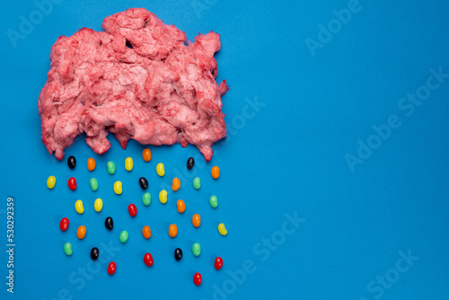 Horizontal image of cloud of homemade pink candy floss raining jelly beans, on blue with copy space