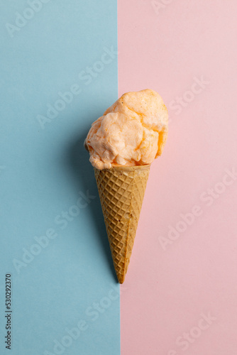 Vertical image of orange homemade ice cream in cone, on blue and pink with copy space