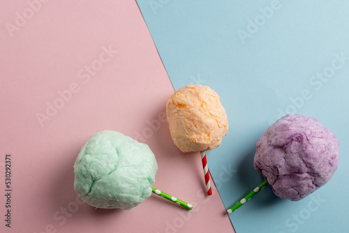 Horizontal image of three sticks of colourful homemade candy floss, on blue and pink with copy space