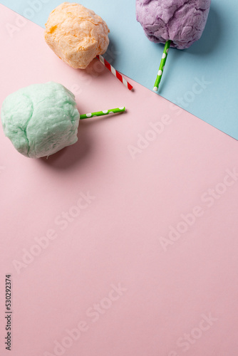 Vertical image of three sticks of colourful homemade candy floss, on blue and pink with copy space
