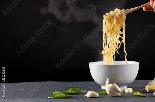 Close up of asian noodles held in chopsticks by caucasian man on black background