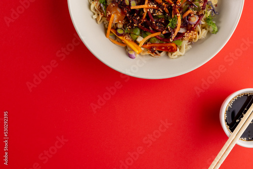 Overhead view of asian wok stir fry, soy sauce and chopsticks with copy space on red background