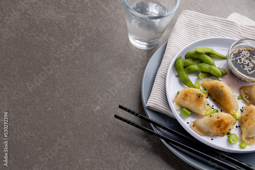 Overhead view of asian dumplings, soy sauce and chopsticks with glass of water on grey background