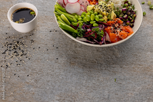Overhead view of hawaiian poke bowl with soy sauce on grey background