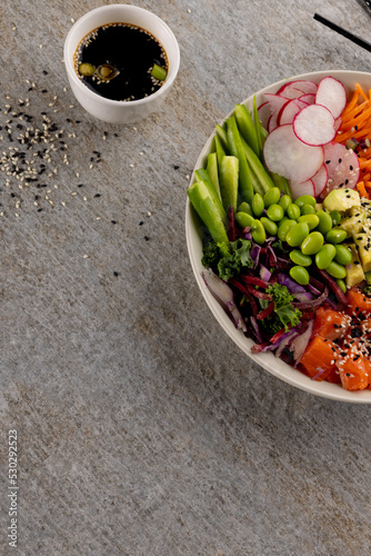 Overhead view of hawaiian poke bowl with chopsticks and soy sauce on grey background