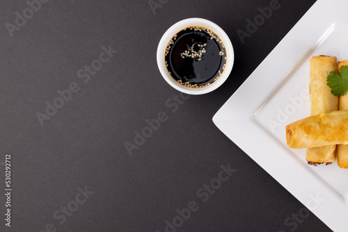 Overhead view of asian spring rolls on white plate and soy sauce with copy space on grey background
