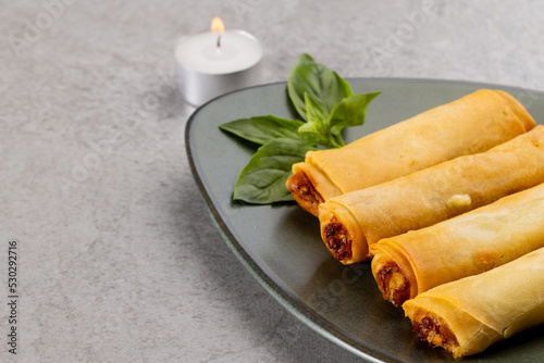 Overhead view of asian spring rolls on grey plate and lit tea candle on grey background