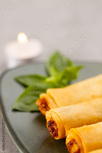 Close up of asian spring rolls on grey plate and lit tea candle on grey background