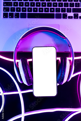 Image of headphones, laptop and smartphone with copy space over neon purple background