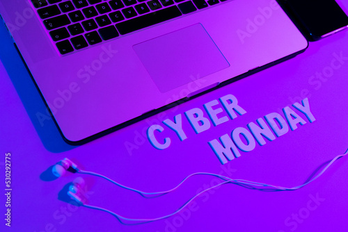 Image of cyber monday text, smartphone, laptop and earphones over neon purple