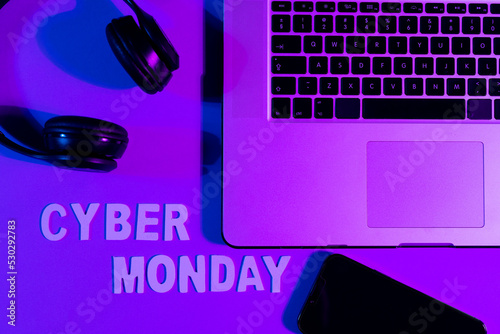Image of cyber monday text, smartphone, laptop and headphones over neon purple background