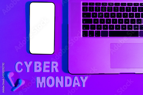 Image of cyber monday text, smartphone with copy space, laptop and earphones over neon purple