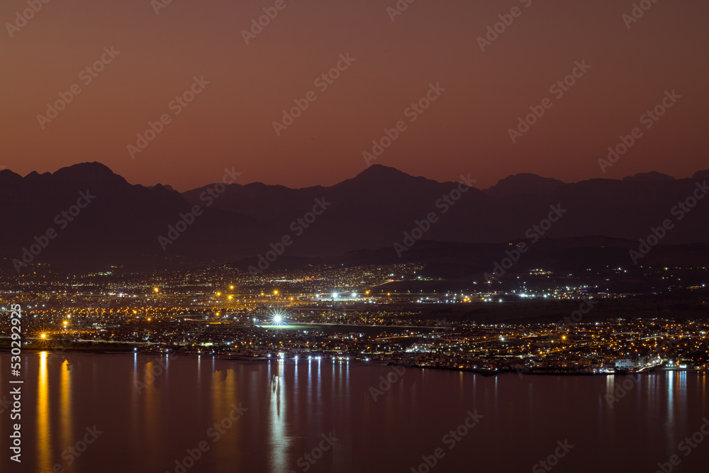 Landscape of sea, sea shore with city lights, mountains, cloudless sky at sunset and horizon