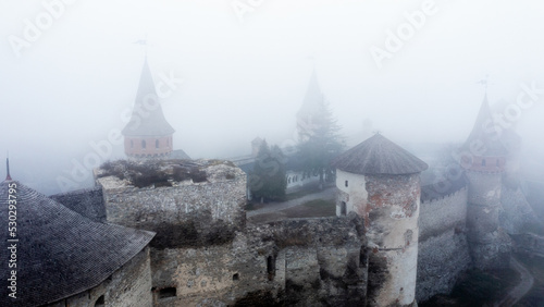 Ancient fortress heritage in Kamenets-podolsky, Ukraine in foggy weather from aerial view. Medieval old castle with authentic towers in clouds from drone