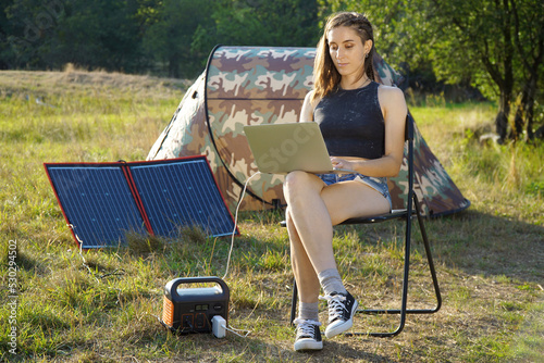 Woman uses solar panel and power station to generate electricity for working on laptop 