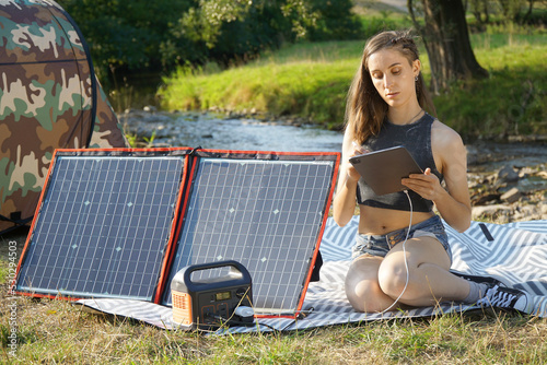 Woman uses solar panel and power station to generate electricity for tablet pc or smartphone