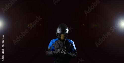 Canvas Print Biker motorcyclist in a protective motorcycle jacket with gloves and a helmet on a dark background
