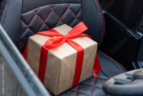 A gift box with a red bow lies on the seat of a children's car, the concept of gifts is loyal to drivers, or delivery.