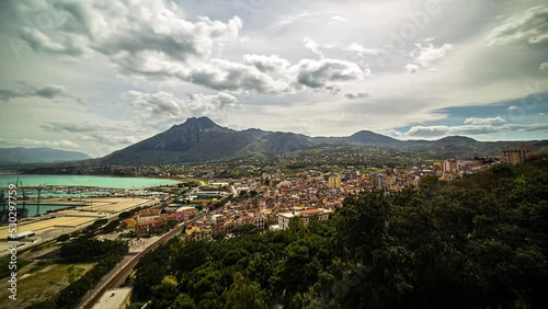 Timelapse of floating clouds over the port city of Termini Imerese in Italy, with buildings and hills in the background on a sunny day photo