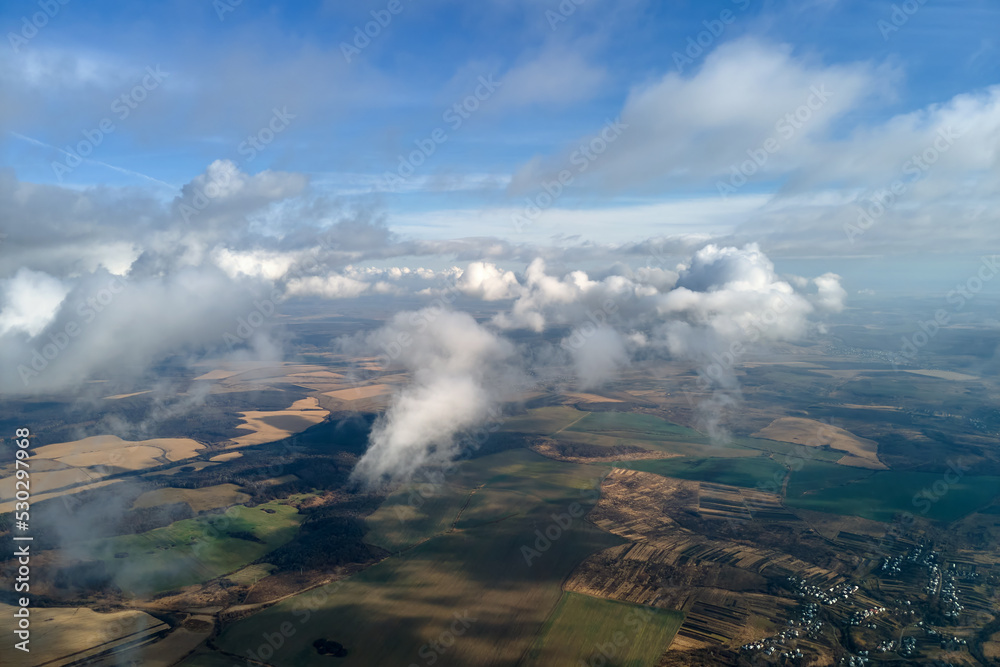 Aerial view from high altitude of distant city covered with puffy cumulus clouds forming before rainstorm. Airplane point of view of cloudy landscape